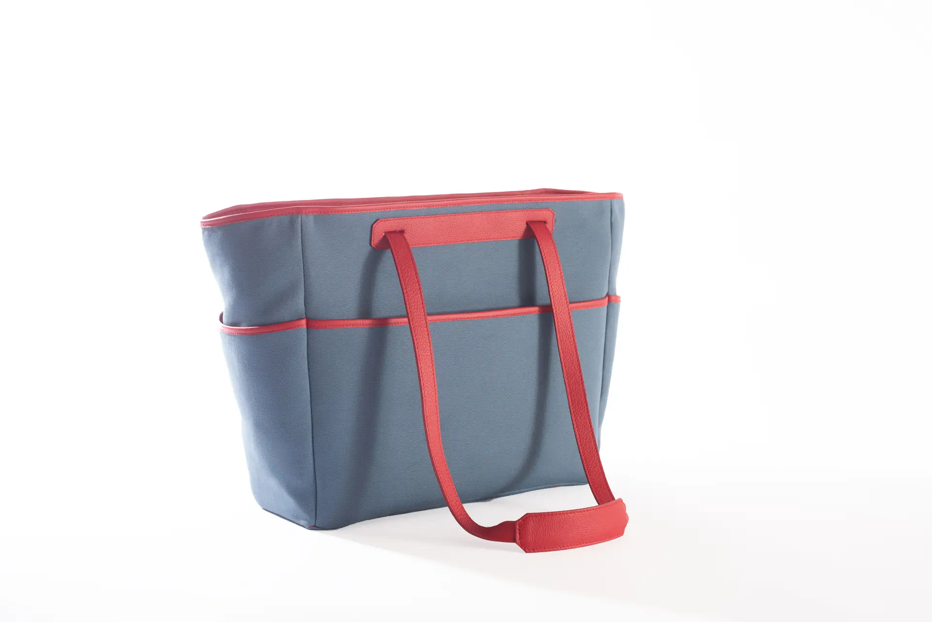 Vista laterale della borsa Liber_TO di Lemanì in blu avio con finiture e manici in pelle rossa, su sfondo bianco. La borsa Lemanì Liber_TO si distingue per il suo stile unico e la praticità, ideale per un look dinamico.