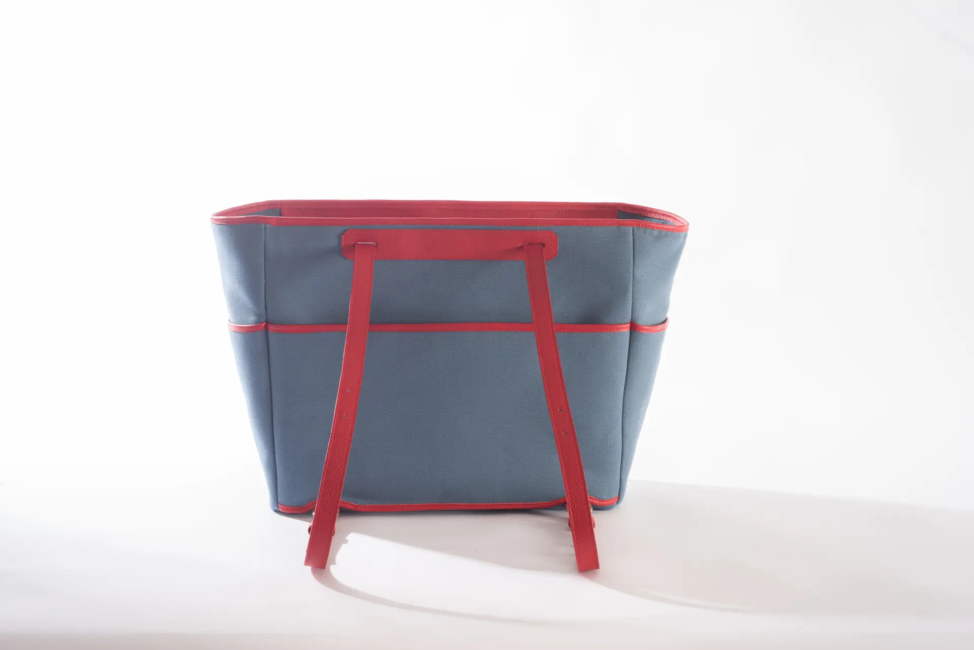 Retro della borsa Liber_TO di Lemanì in cotone blu avio con dettagli e spallacci regolabili in pelle rossa, su sfondo bianco. Questa borsa a mano Lemanì Liber_TO offre un contrasto cromatico audace e un design funzionale per l'uso quotidiano.